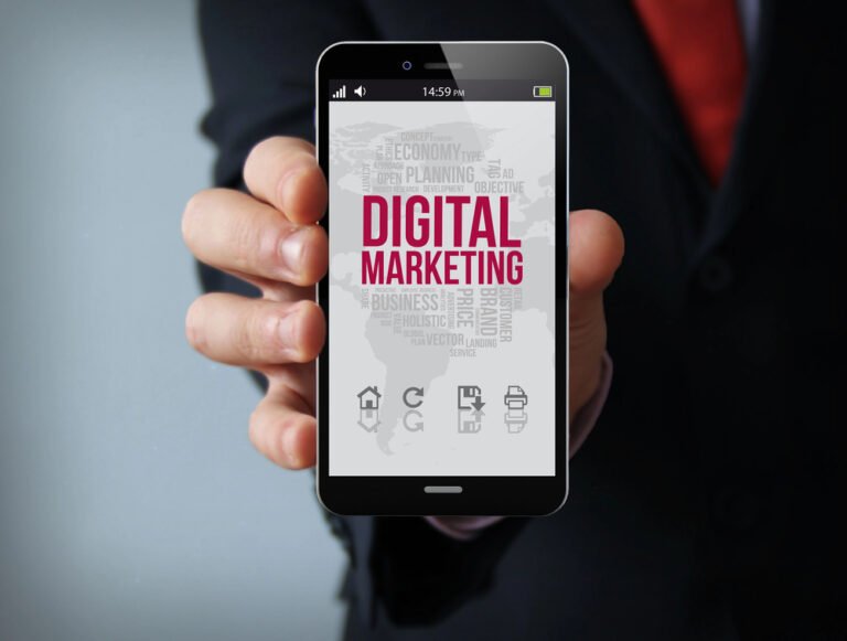Mano che tiene telefono con app digital marketing, scritta rossa su sfondo bianco con termini correlati
