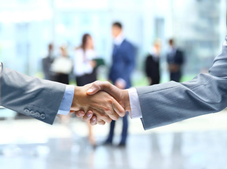 Stretta di mano professionale tra business partners con team sfocato in ufficio moderno