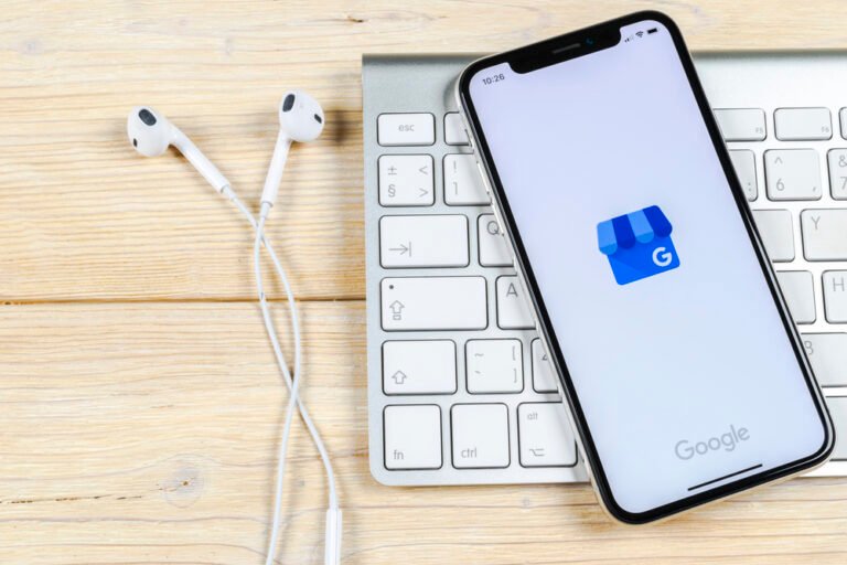 Smartphone con app Google My Business su scrivania con tastiera wireless e auricolari bianchi