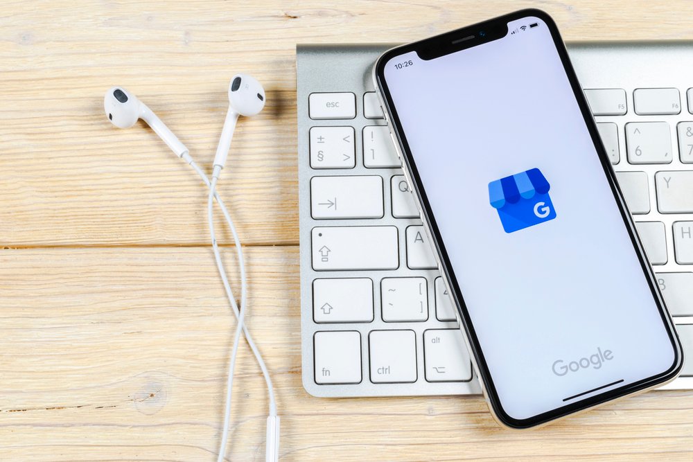 Smartphone con app Google My Business su scrivania con tastiera wireless e auricolari bianchi